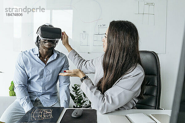 Architekt passt Virtual-Reality-Headset für Kollegen an  die im Büro am Schreibtisch sitzen