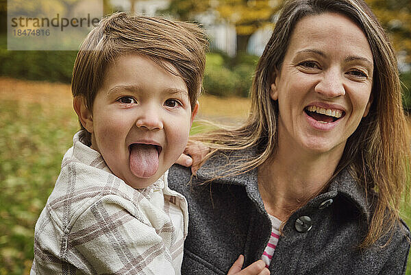 Sohn streckt glücklicher Mutter im Park die Zunge heraus