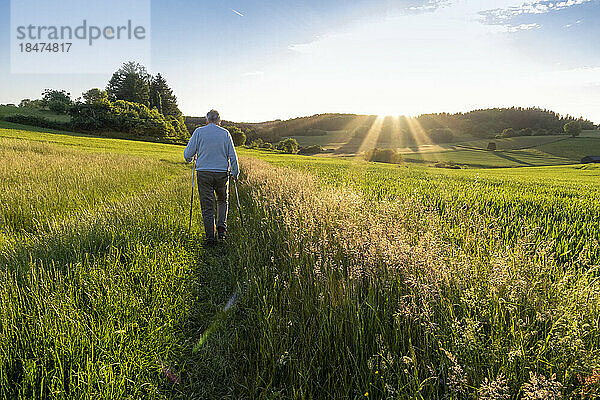 Aktiver älterer Mann  der bei Sonnenuntergang im Feld spaziert