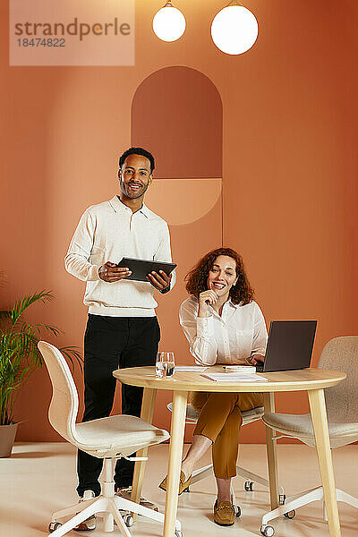 Junger Geschäftsmann hält Tablet-PC in der Hand  während Kollege am Schreibtisch im Büro sitzt