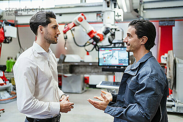 Lächelnder Ingenieur im Gespräch mit Techniker in der Roboterfabrik
