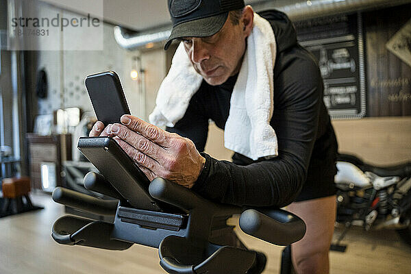 Mann benutzt Smartphone  sitzt auf Heimtrainer im Fitnessstudio
