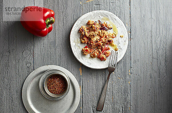 Rohe Paprika  Chilipulver und ein Teller mit verzehrfertigem Couscous