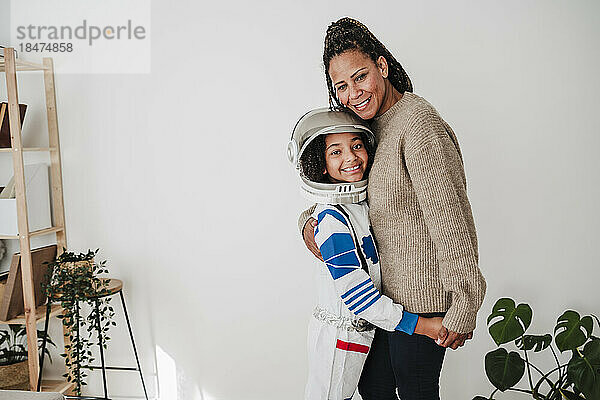 Lächelndes Mädchen im Raumanzug umarmt Mutter zu Hause