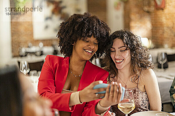 Glückliche Frau teilt Smartphone mit Freund im Restaurant