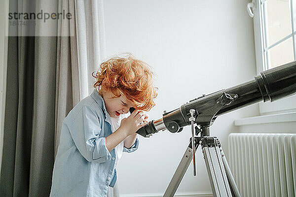 Neugieriger Junge schaut zu Hause durch das Teleskop