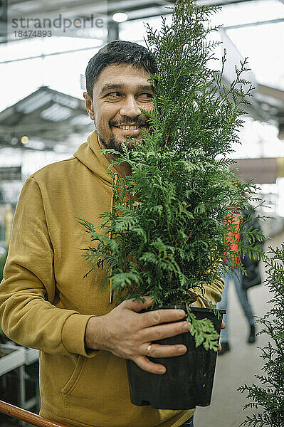 Glücklicher Mann hält Topfpflanze im Laden