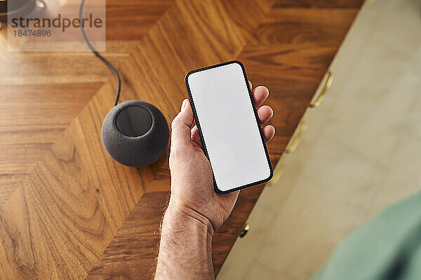 Mann verbindet Telefon mit leerem Bildschirm mit intelligentem Lautsprecher auf der Küchentheke