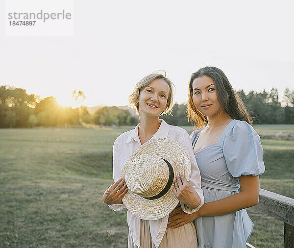 Happy friends standing in park at sunset