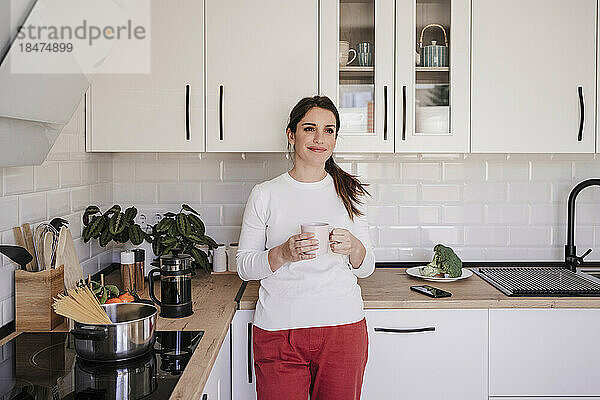 Lächelnde Frau hält Kaffeetasse in der Küche