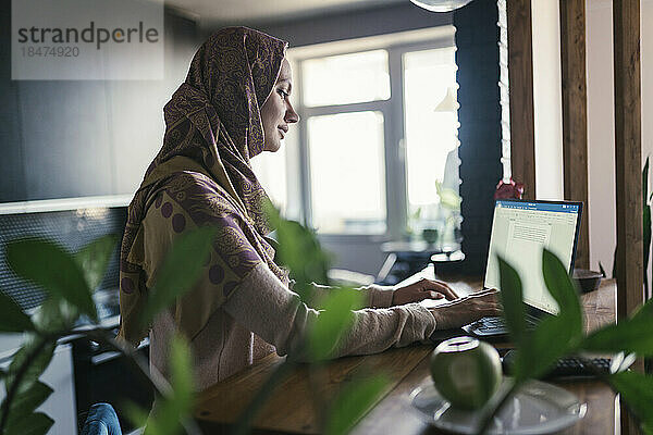 Freiberufler mit Hijab arbeitet im Heimbüro am Laptop
