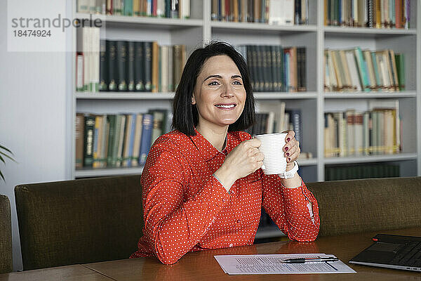 Glückliche Geschäftsfrau mit Kaffeetasse am Schreibtisch