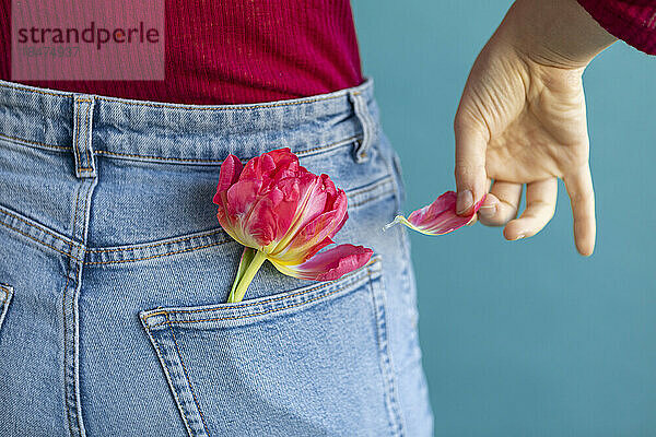 Frau pflückt Tulpenblätter aus der Jeanstasche vor grünem Hintergrund