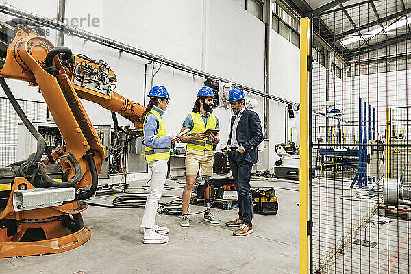 Ingenieur mit Kollegen  die Schutzhelm tragen  diskutieren in der Fabrik