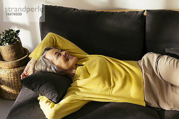 Lächelnde reife Frau entspannt sich auf dem Sofa im Wohnzimmer