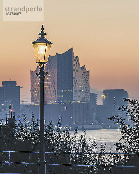 Deutschland  Hamburg  Straßenlaterne leuchtet vor der Elbphilharmonie  die in der Abenddämmerung im Hintergrund steht