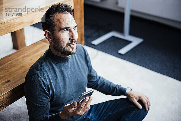 Businessman with mobile phone sitting on floor in office