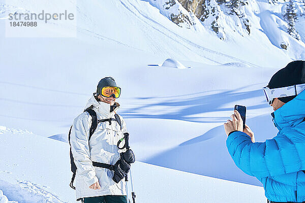 Reifer Mann fotografiert Frau mit Smartphone im Schnee