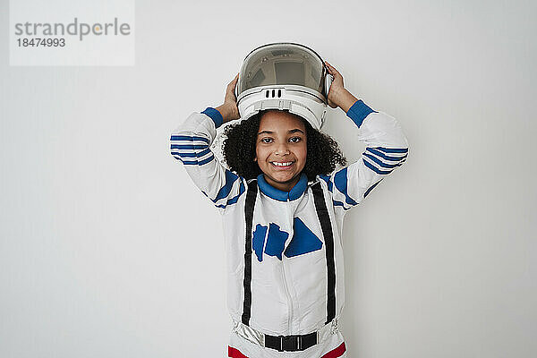 Smiling girl wearing space helmet in front of white wall