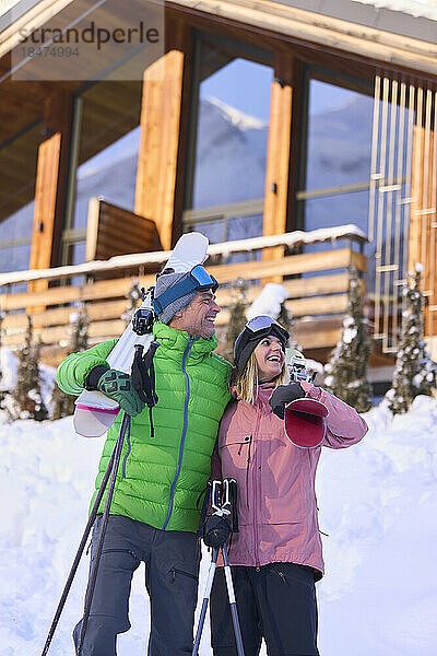 Glücklicher Mann und Frau stehen mit Skiern im Schnee