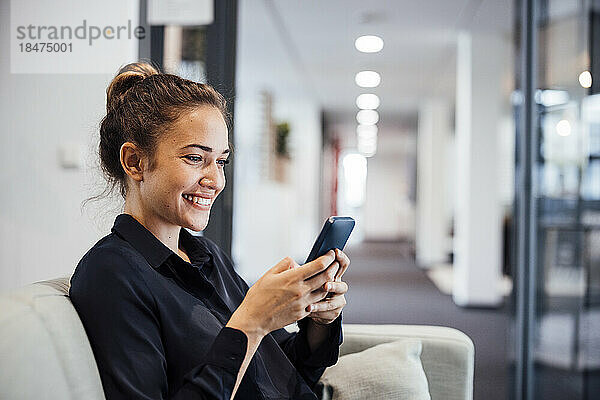 Glückliche Geschäftsfrau benutzt Smartphone auf dem Sofa im Büro