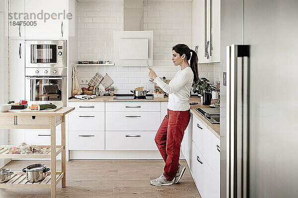 Frau benutzt Tablet-PC und steht in der Küche