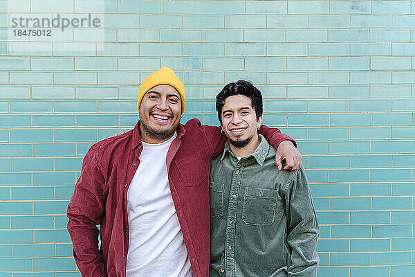 Lächelnder Mann mit Bruder steht vor einer türkisfarbenen Ziegelwand