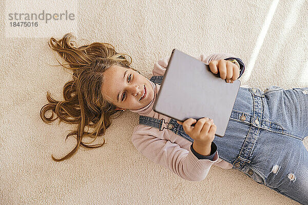 Happy girl using tablet PC lying on carpet at home