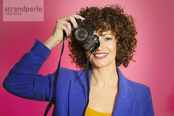 Lächelnde Frau fotografiert mit der Kamera vor magentafarbenem Hintergrund