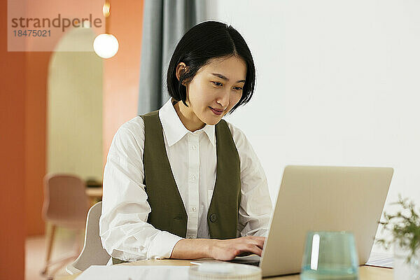 Lächelnde Geschäftsfrau mit kurzen Haaren  die im Büro am Laptop arbeitet