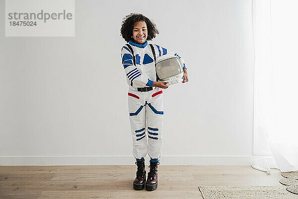 Smiling girl holding space helmet standing in front of white wall