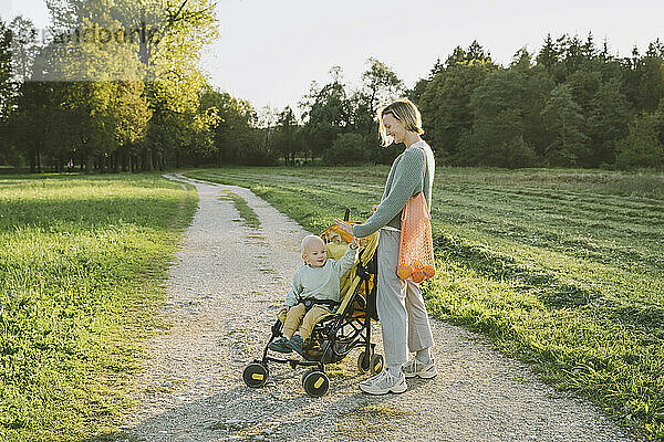 Frau mit Sohn sitzt im Kinderwagen auf Fußweg