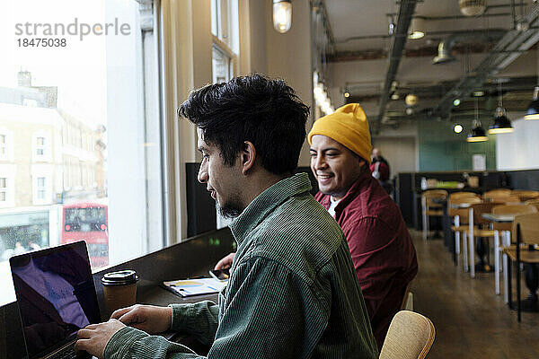 Junger Freiberufler arbeitet mit Bruder am Laptop im Café