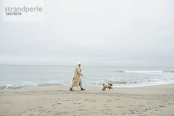 Frau spaziert mit Hund in Ufernähe am Strand