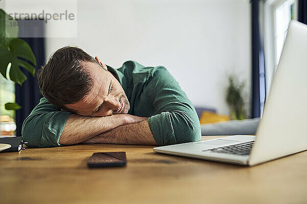 Überarbeiteter Mann schläft auf Armen am Schreibtisch