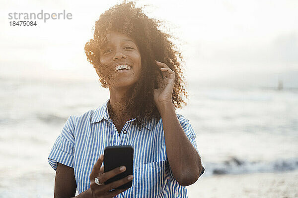 Glückliche Frau mit Smartphone vor dem Meer bei Sonnenuntergang