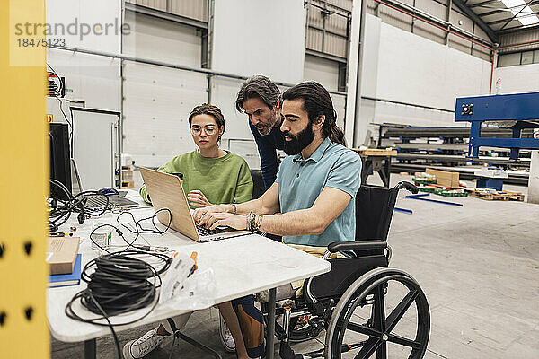 Ingenieur sitzt im Rollstuhl und arbeitet mit Kollegen in der Fabrik