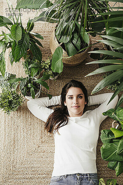 Frau mit Händen hinter dem Kopf liegt inmitten von Pflanzen auf einem Teppich