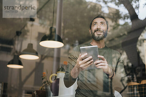 Glücklicher reifer Mann mit Tablet-PC durch Glas gesehen