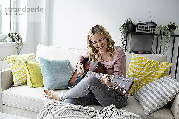 Glückliche reife Frau  die zu Hause auf dem Sofa Gitarre spielt