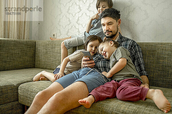 Vater teilt Smartphone mit Söhnen  die zu Hause auf dem Sofa sitzen