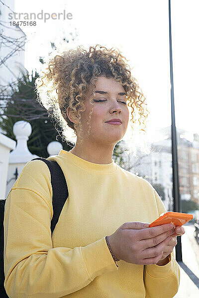 Junge Frau mit geschlossenen Augen hält Smartphone in der Hand