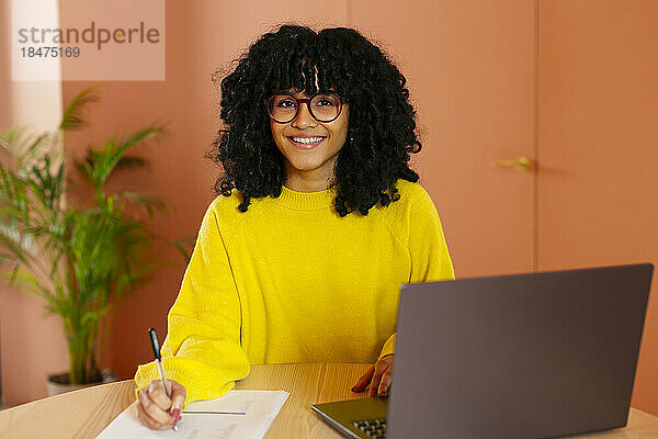Selbstbewusste junge Frau sitzt mit Laptop am Schreibtisch im Büro