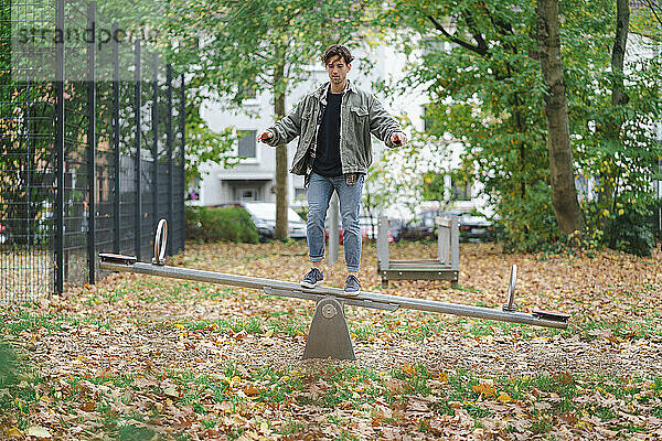 Junger Mann steht und balanciert auf Wippe im Park