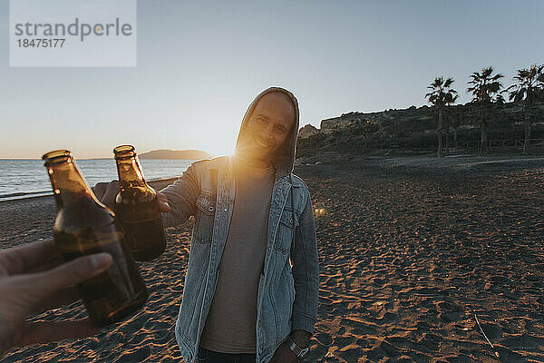 Glücklicher Mann  der bei Sonnenuntergang mit einem Freund eine Bierflasche anstößt