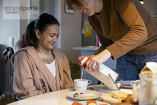 Weibliche Pflegekraft gießt Milch in eine Tasse für eine Frau mit Behinderung zu Hause