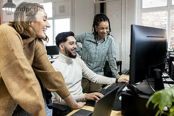 Glückliche Geschäftsleute  die im Büro auf den Desktop-PC schauen