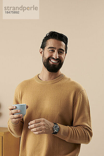 Glücklicher Mann hält Kaffeetasse vor der Wand