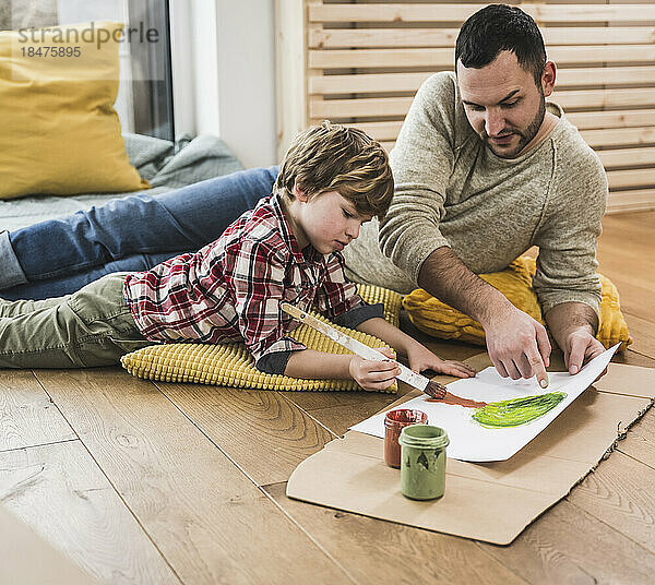 Vater spricht mit Sohn und malt zu Hause einen Baum