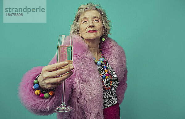 Ältere Frau hält Champagnerkurs vor türkisfarbenem Hintergrund